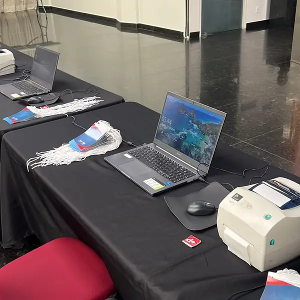 Posto de credenciamento com notebook, impressora de crachás e cordões prontos para o público