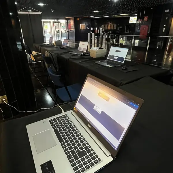 Notebook de credenciamento em operação, com o salão do evento ao fundo